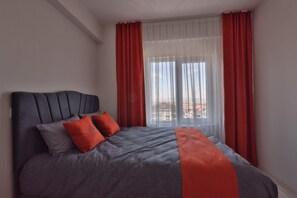 Un dormitorio con cama, cabecera y ventana con cortinas.