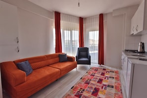 A modern living room with a sofa, a chair, and a kitchen area with a kettle. - H&M SUIT CAPPADOCIA (Merkez)