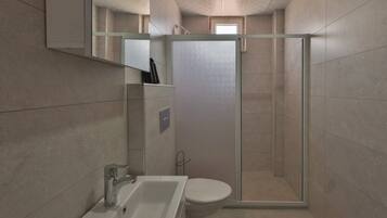 Un bany modern amb un box de dutxa de vidre, un lavabo blanc i un vàter.