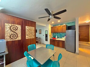 A compact kitchen with wooden cabinets, a stainless steel refrigerator, and a dining area with a metal table and blue chairs. - Soundproof apartment on the boardwalk with a balcony (half a block from the beach) (Puerto Vallarta)