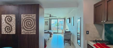 A hotel room with a balcony, a kitchenette, and a hallway leading to another room.