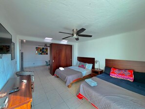 A hotel room with two beds, a desk, a chair, a ceiling fan, and a wall with a colorful tapestry. - Soundproof apartment on the boardwalk with a balcony (half a block from the beach) (Puerto Vallarta)