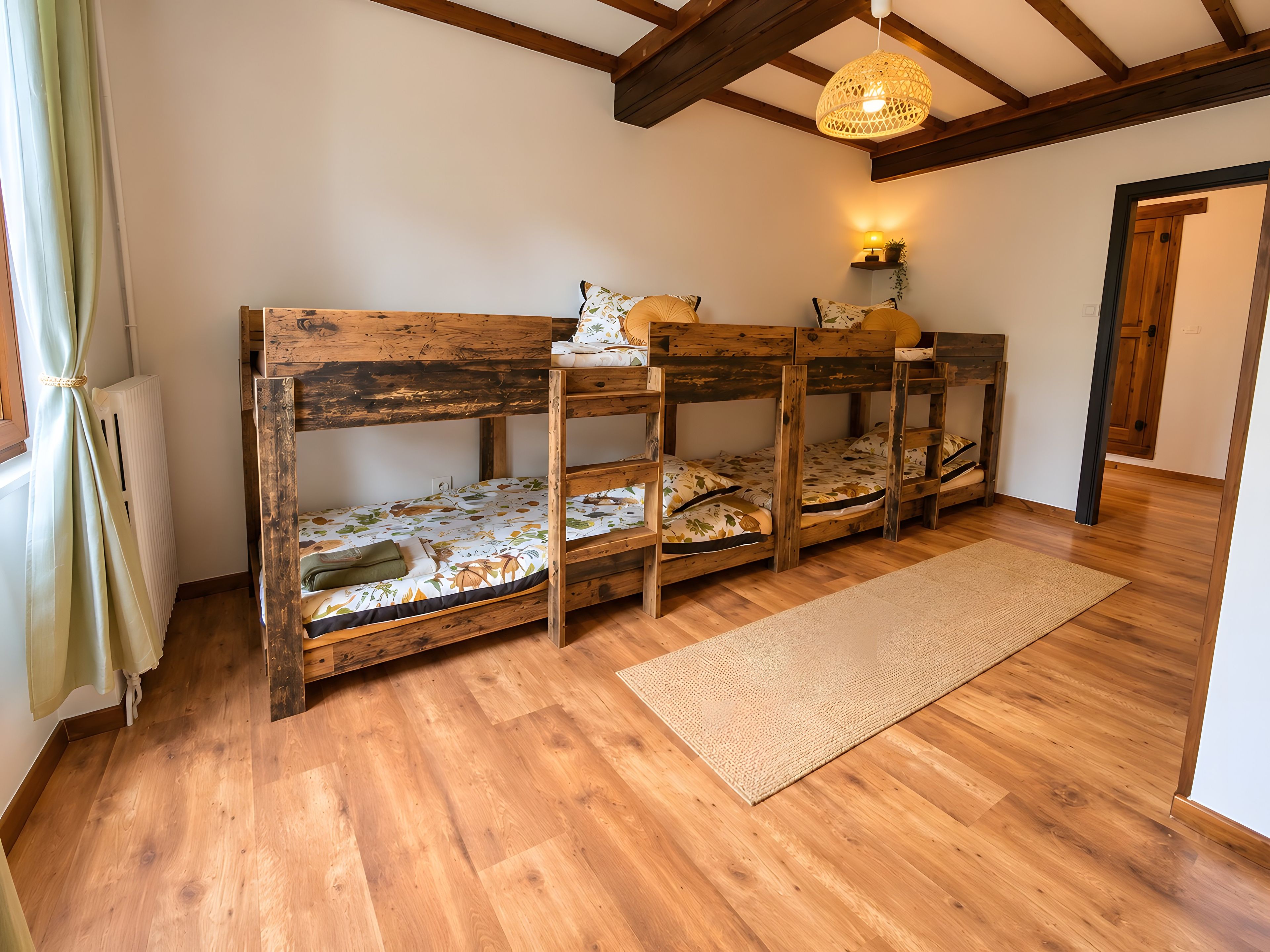 A room with four bunk beds, a wooden floor, a woven rug, and a hanging light fixture.