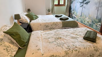 Une chambre avec deux lits, une fenêtre avec des rideaux, un tableau au mur et une petite plante en pot.