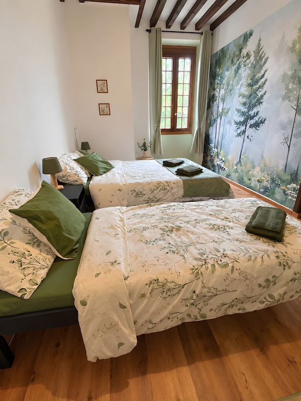 Een kamer met twee bedden, een raam met gordijnen, een wanddecoratie en een kleine potplant.