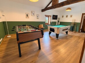 Ein Raum mit einer Tischfußballplatte, einem Billardtisch und einer Dartscheibe.