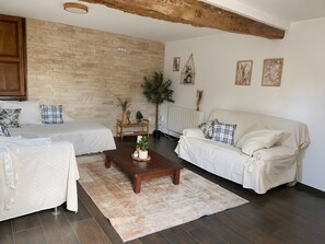 Ein Zimmer mit zwei Betten, einem Holztisch, einer Heizung und einer Steinwand.