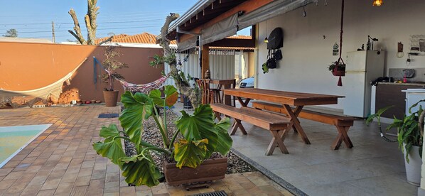 A patio area with a wooden table and benches, a hammock, and potted plants.