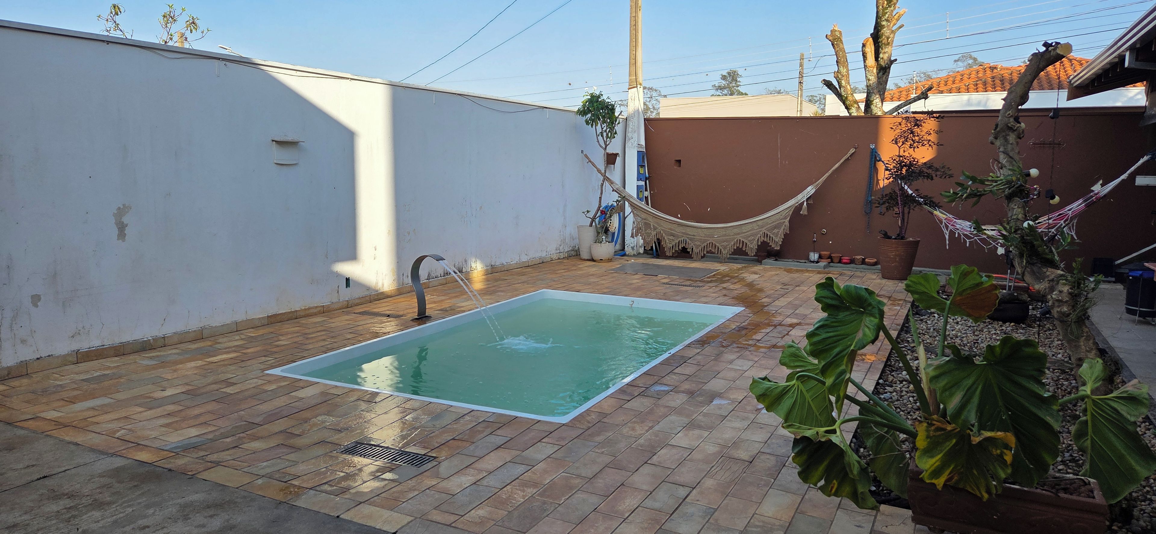 Una piscina rectangular con un solo grifo, rodeada por un patio con baldosas.