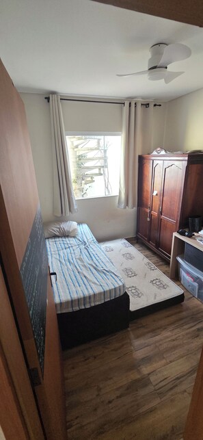 A compact room with a bed, a wardrobe, a window, and a ceiling fan.