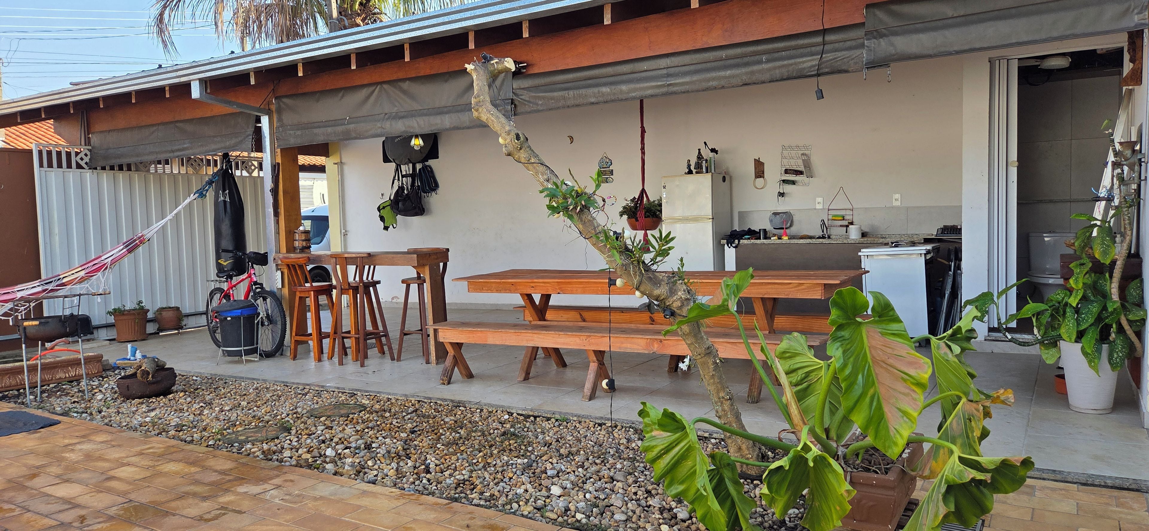 An outdoor patio area with a wooden table and chairs, a hammock, and various potted plants.