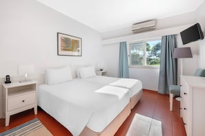 Une chambre d’hôtel avec un grand lit, une table de chevet avec une lampe, un téléviseur à écran plat fixé au mur et une fenêtre avec des rideaux.