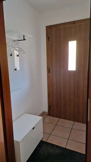Een kamer met een houten deur, een witte muur en een klein raam.
