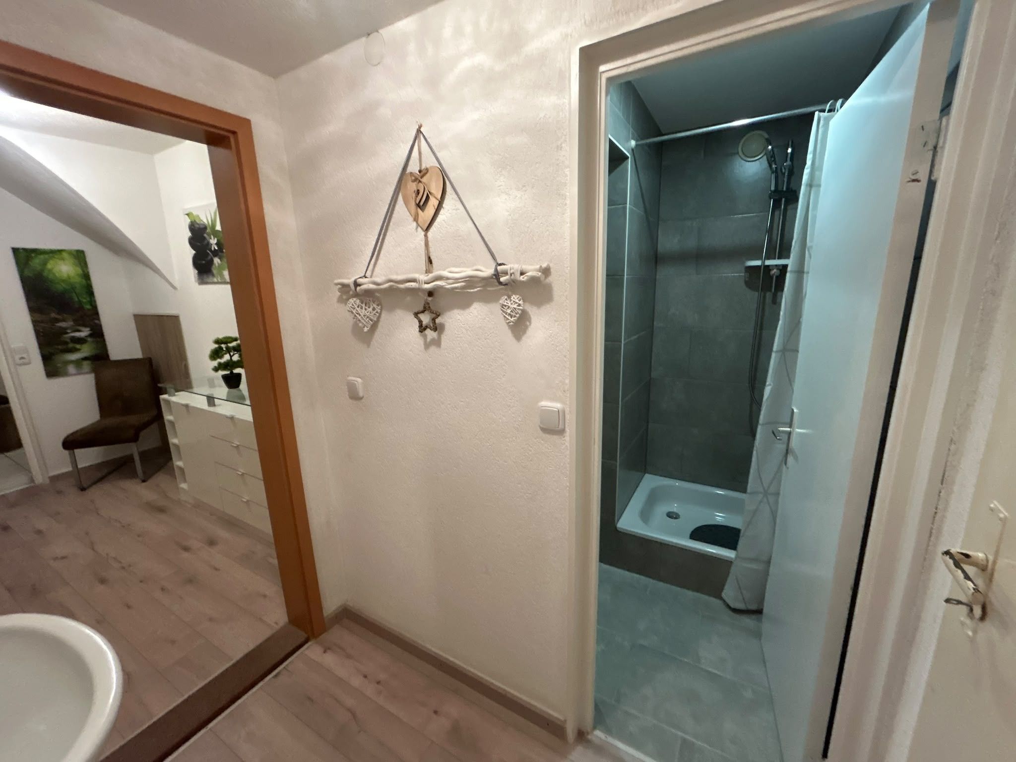 Een badkamer met een glazen douchecabine, een witte wastafel en een decoratieve wandversiering.