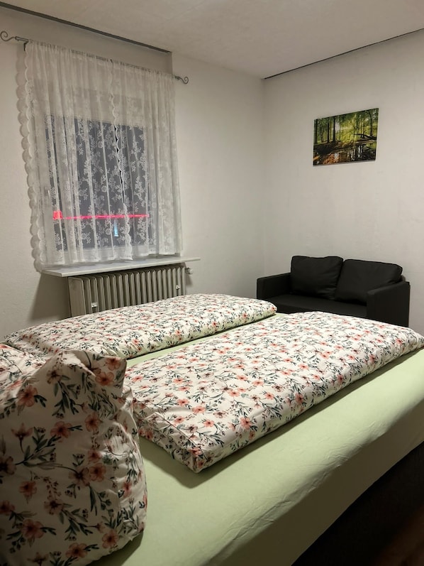 Een kamer met een bed, een radiator, een raam met gordijnen, een zwarte bank en een foto aan de muur.