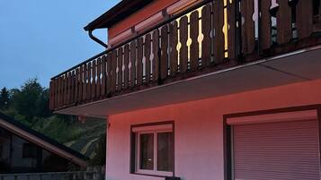 A two-story building with a balcony, outdoor seating, and a garage door.