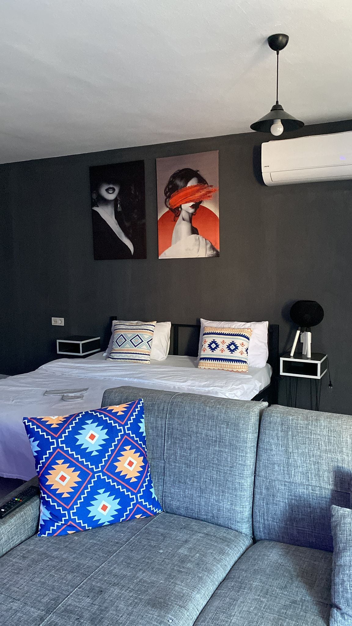 Un dormitorio moderno con una cama, un sofá y dos obras de arte colgadas en la pared.