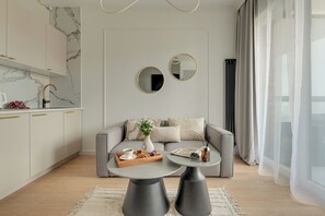 A modern living room with a sofa, coffee table, and two side tables. There is a kitchen area with marble backsplash and a sink. - Kapitanat Riverside by Downtown Apartments (Gdańsk)