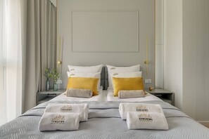 Habitació d'hotel amb un llit ben fet, dos almoinos amb un logotip, una taula de nit amb un ram de flors i una làmpada penjada a la paret.