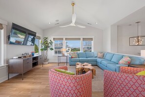 A spacious living room with a sectional sofa, a flat-screen TV mounted on the wall, and a ceiling fan. - Shore Thing: Oceanside, Private Pool, Hot Tub (Corolla)