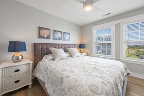 A bedroom with a bed, nightstands, lamps, framed artwork, and a window with blinds. - Shore Thing: Oceanside, Private Pool, Hot Tub (Corolla)