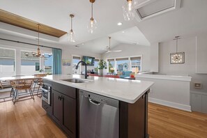 A modern kitchen with a large island, stainless steel appliances, and pendant lighting. - Shore Thing: Oceanside, Private Pool, Hot Tub (Corolla)