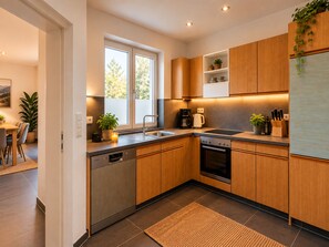 A modern kitchen with wooden cabinets, stainless steel appliances, and a window providing natural light. - Apartment 'Felix Living 11 – Lusenblick - Großzügige Wohnung für bis zu 8 Personen' (Mauth)