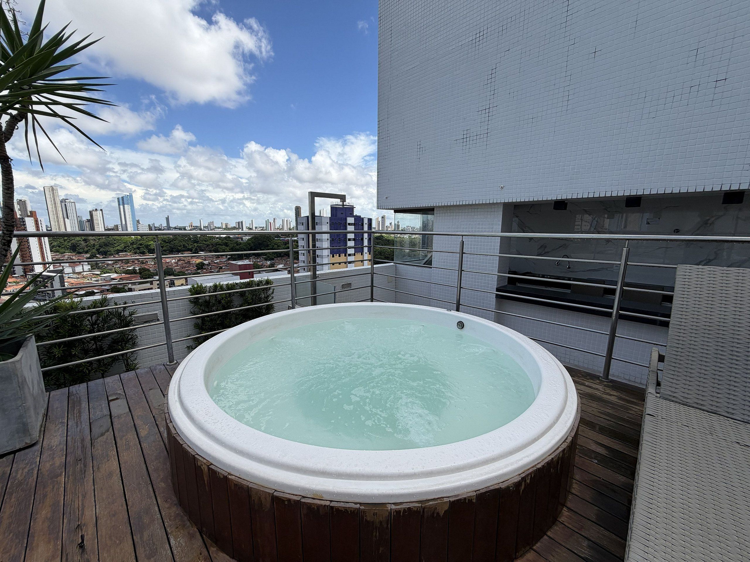 Una azotea con jacuzzi, vista panorámica de la ciudad y un edificio moderno con fachada de azulejos.