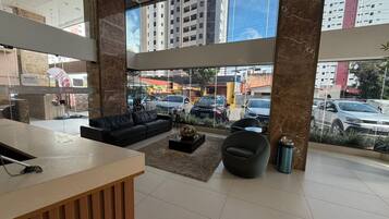Un vestíbulo moderno con un mostrador de recepción, asientos de cuero y grandes ventanales que ofrecen vistas a la calle y edificios.