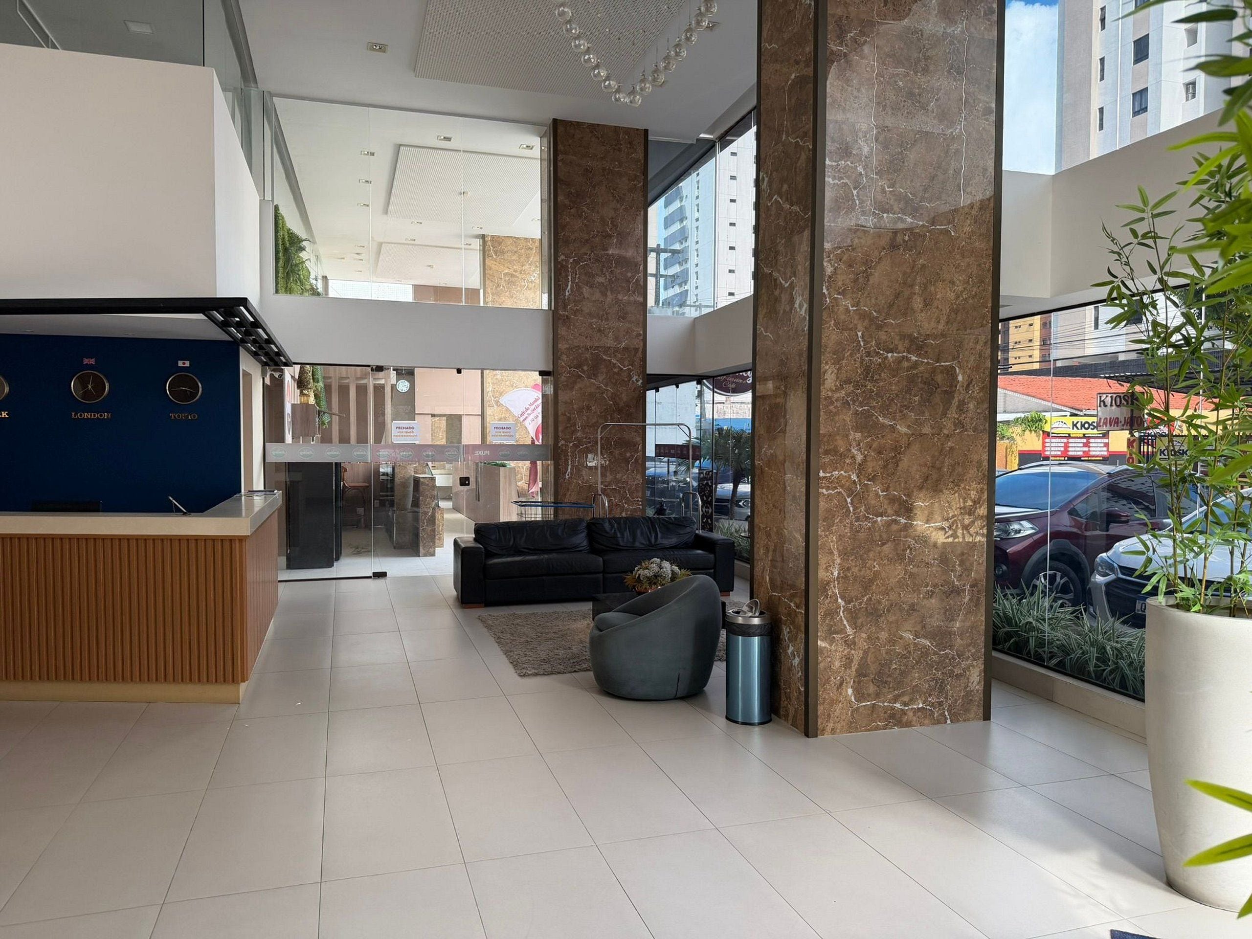 A modern lobby with a reception desk, seating area, and large windows offering a view of the street.