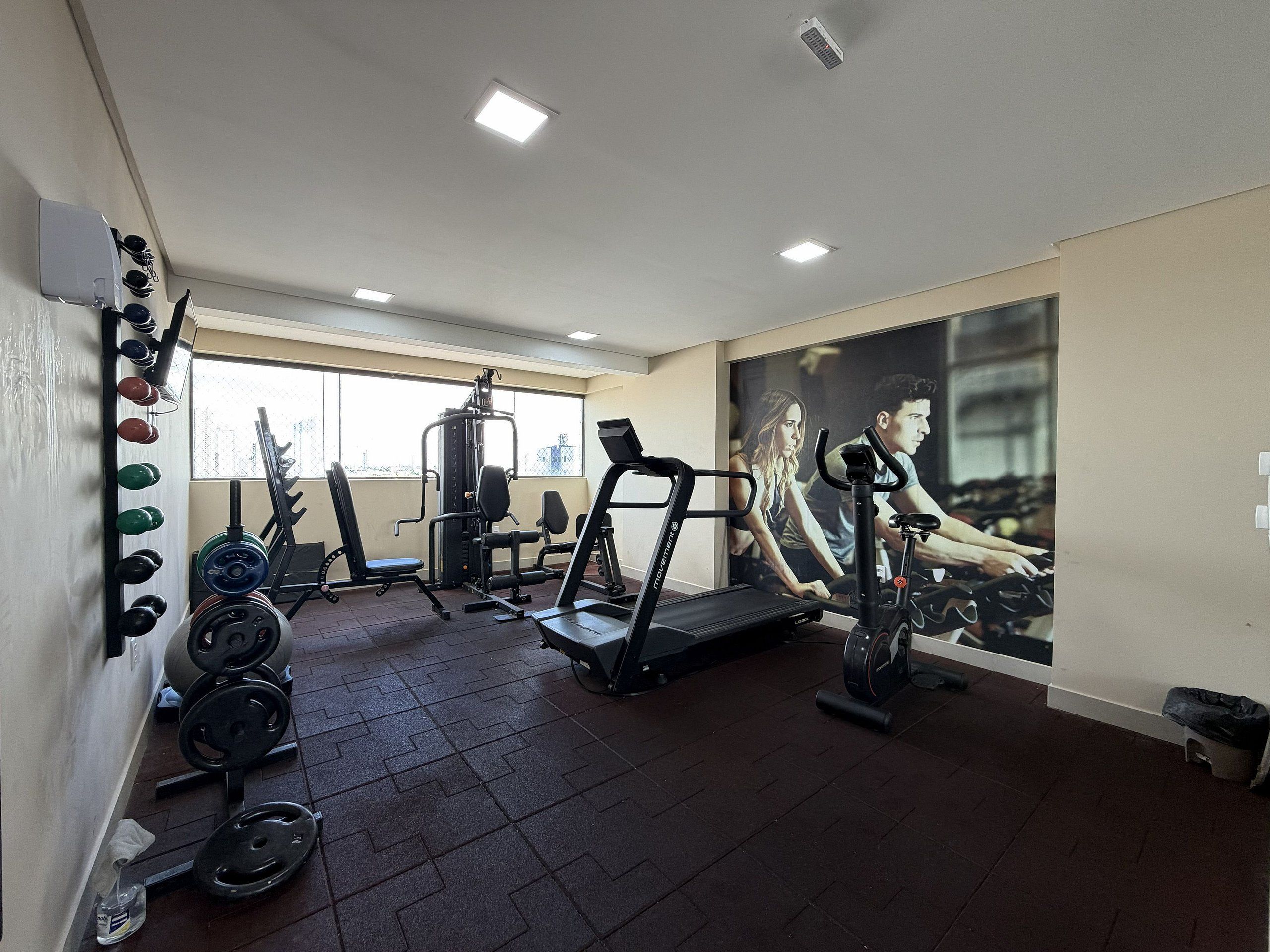Un gimnasio con equipo de levantamiento de pesas, cintas de correr y un cartel grande en la pared.