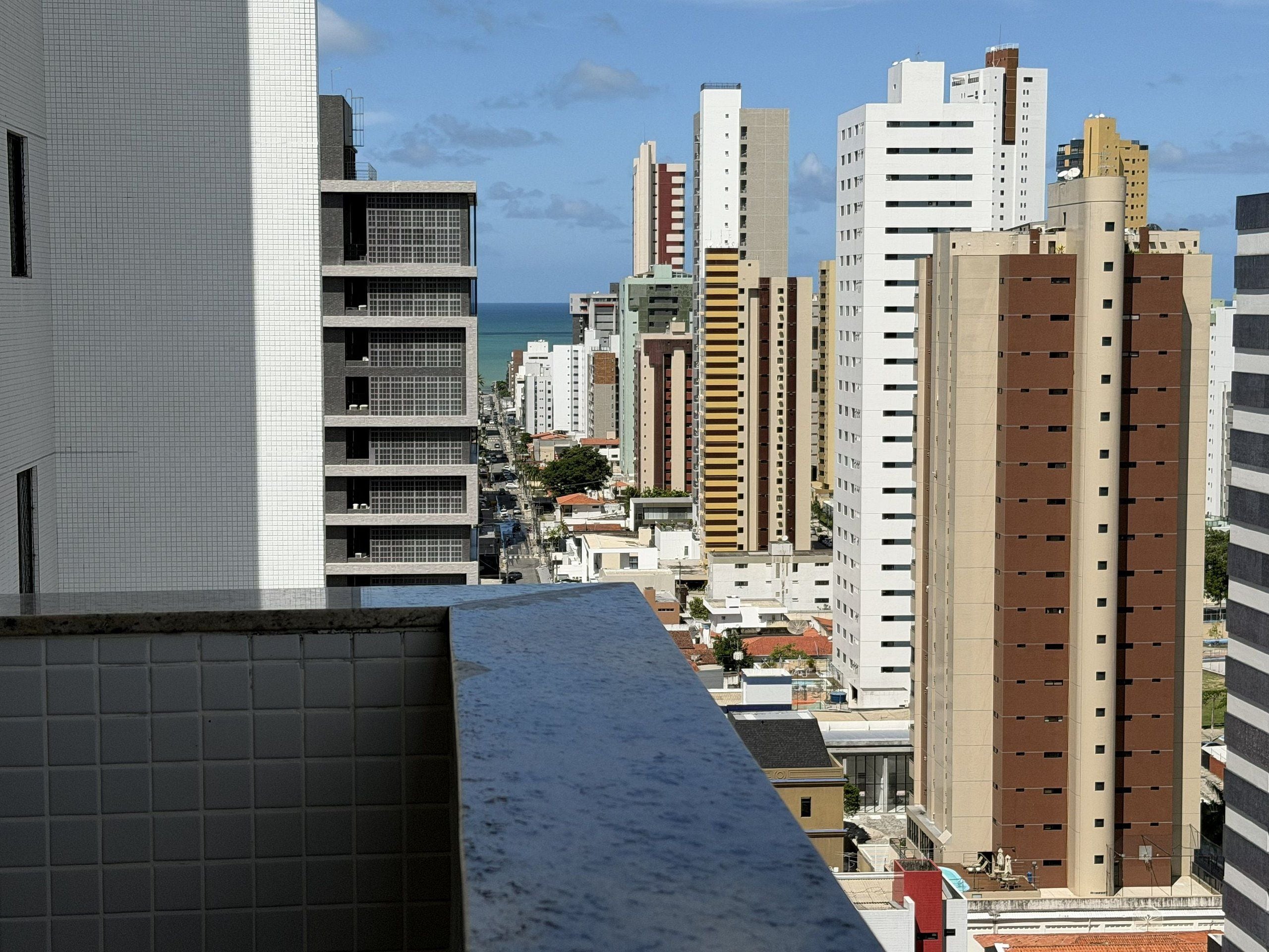 Zona urbana com arranha-céus e vários edifícios, incluindo um edifício branco de destaque com fachada em grade e um edifício marrom com padrão de listras verticais.