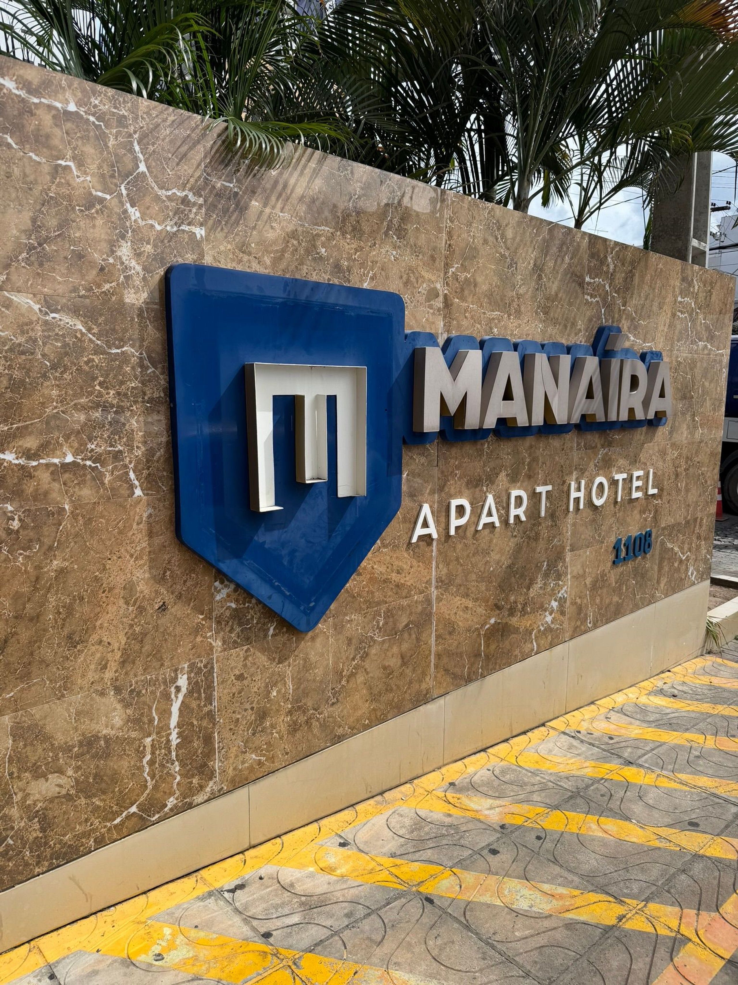 Letrero del Manaira Apart Hotel con fondo de pared de mármol y logotipo azul.