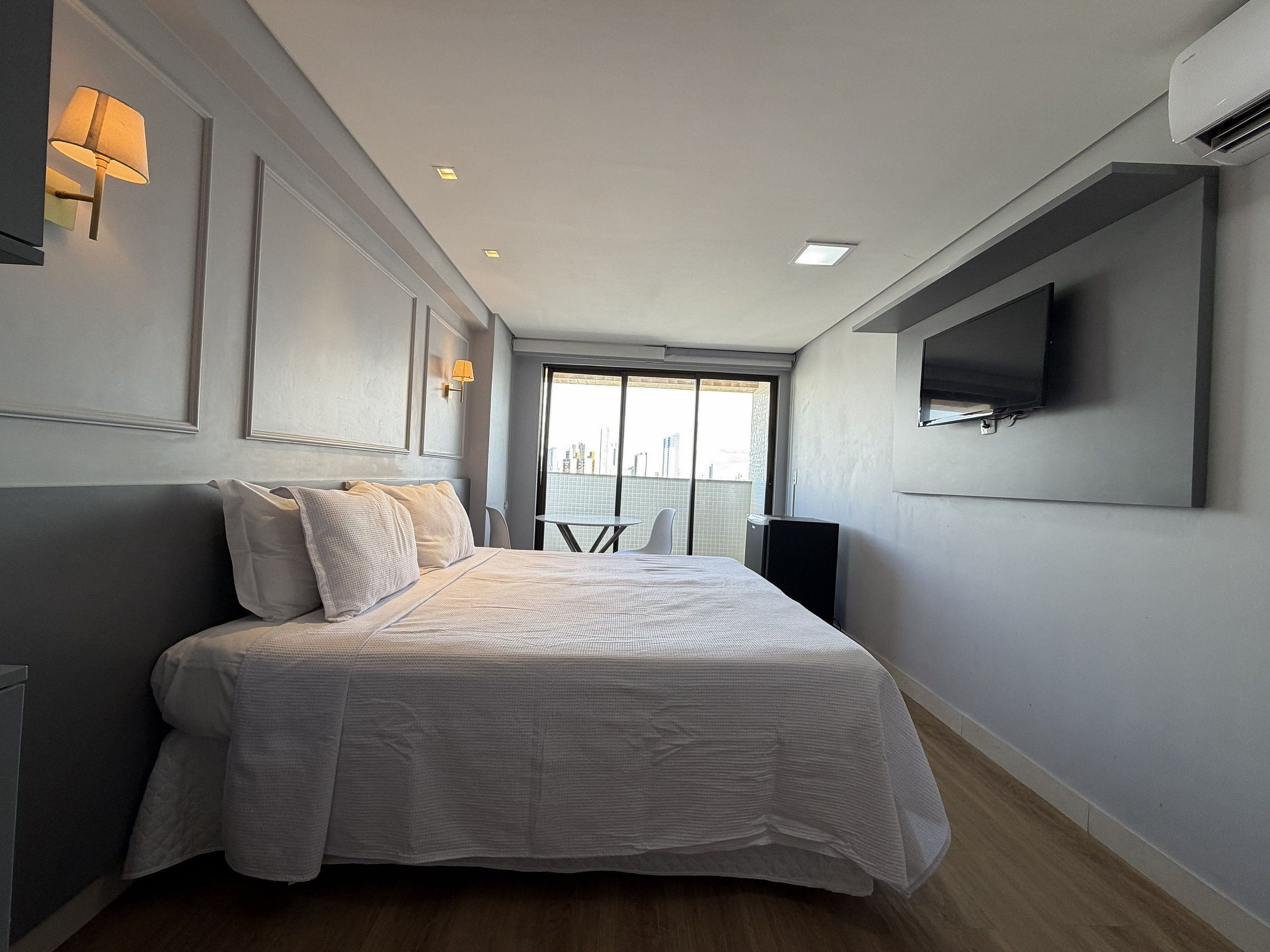 Una habitación de hotel moderna con una cama grande, un televisor de pantalla plana en la pared y vistas a la ciudad a través del ventanal.