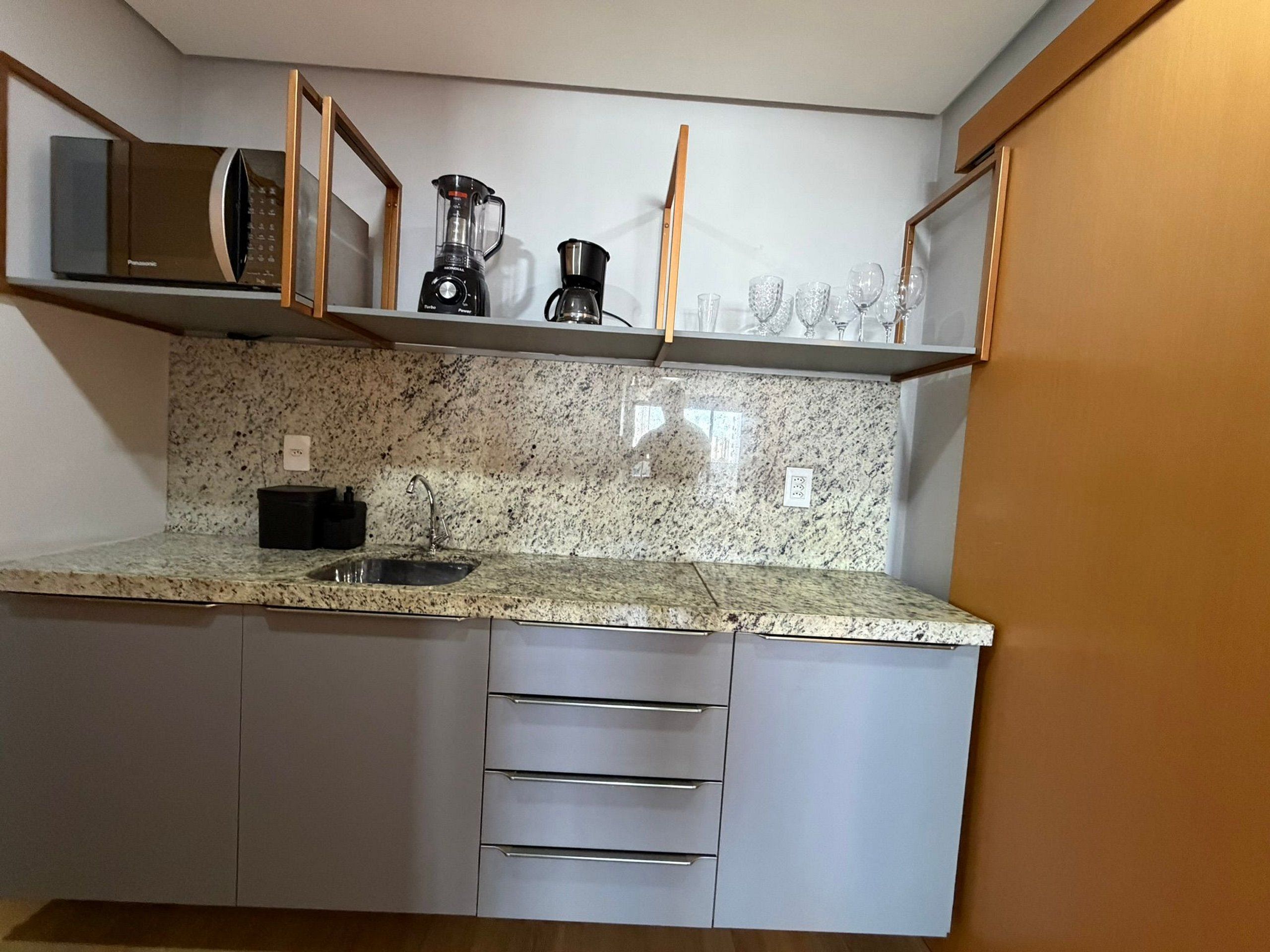 Cocina con encimeras de granito, un lavamanos, una cafetera, una licuadora y un microondas.