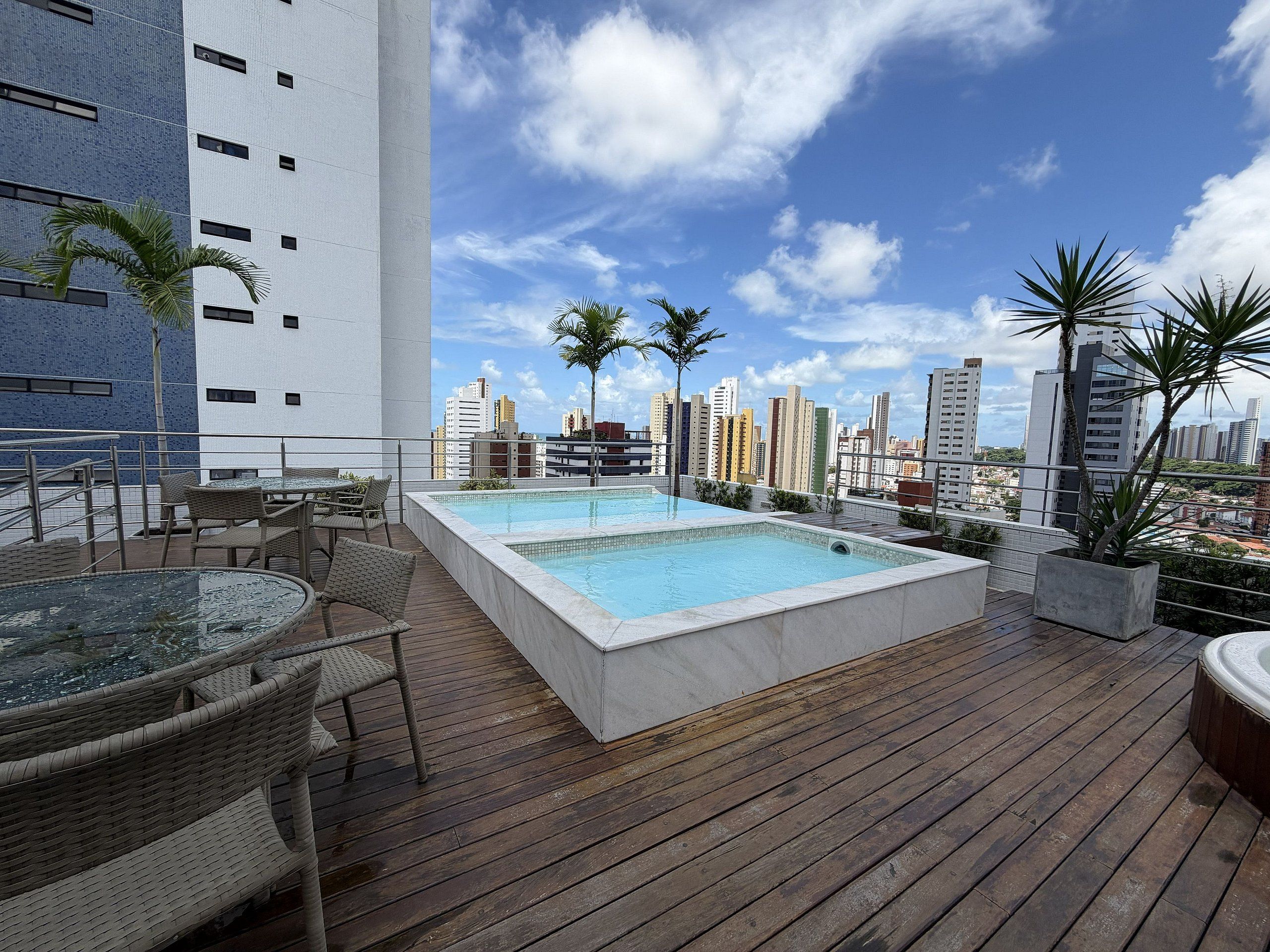 Un área de piscina en la azotea con vista a un horizonte urbano, incluyendo rascacielos y palmeras.
