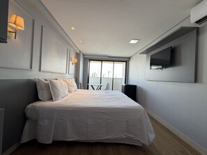 A modern hotel room with a large bed, a flat-screen TV mounted on the wall, and a city view through the window. - Manaíra Apart Hotel  (João Pessoa)
