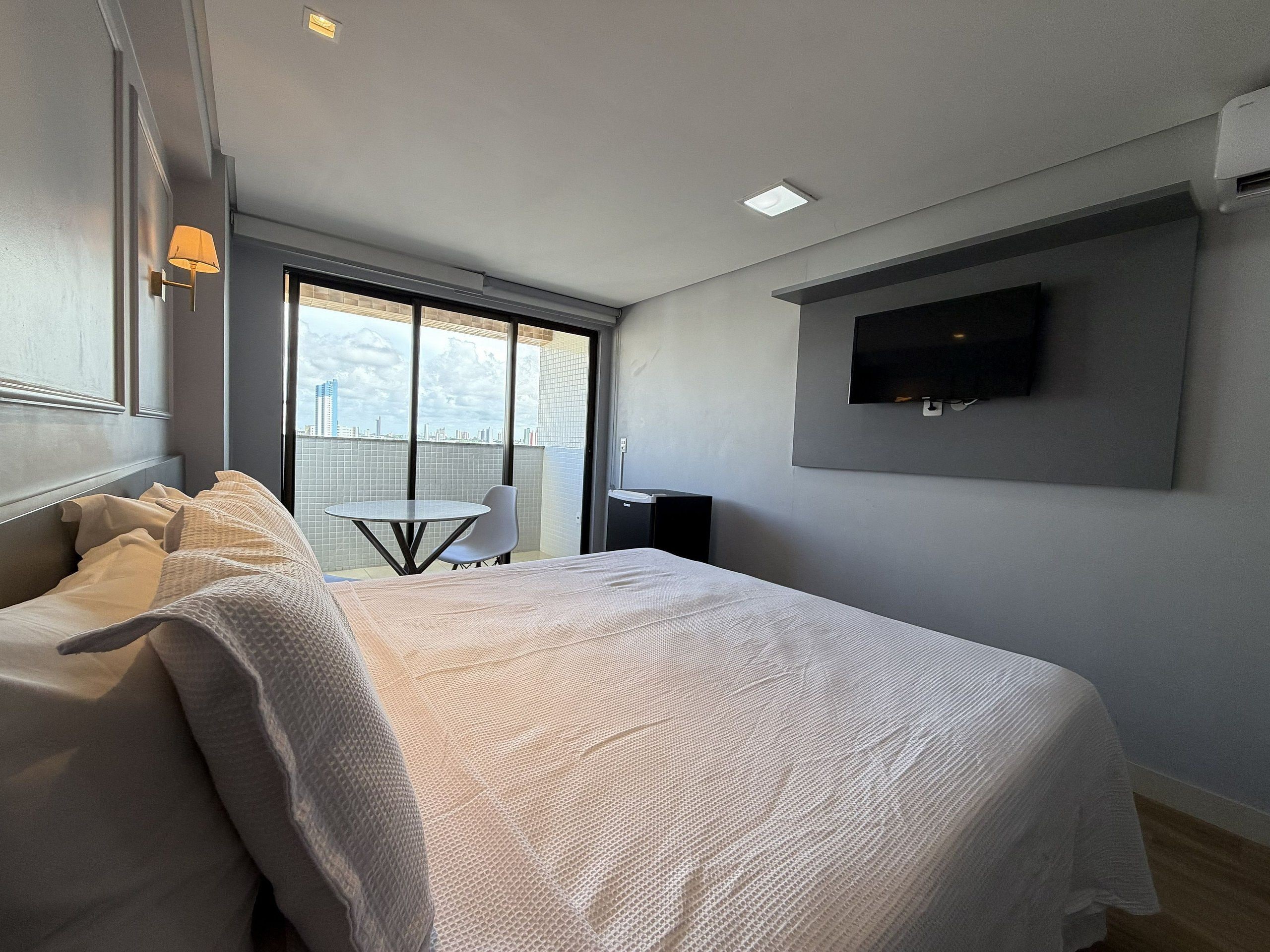 Ein modernes Hotelzimmer mit einem großen Bett, einem kleinen Tisch und einem an der Wand montierten Fernseher.