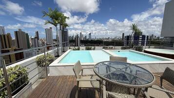 Un espace piscine sur le toit, comprenant deux piscines, une table et des chaises, le tout offrant une vue panoramique sur la ville.