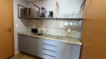 Eine kompakte Küche mit einer Granitarbeitsplatte, einer eingebauten Kaffeemaschine und einer Mikrowelle.