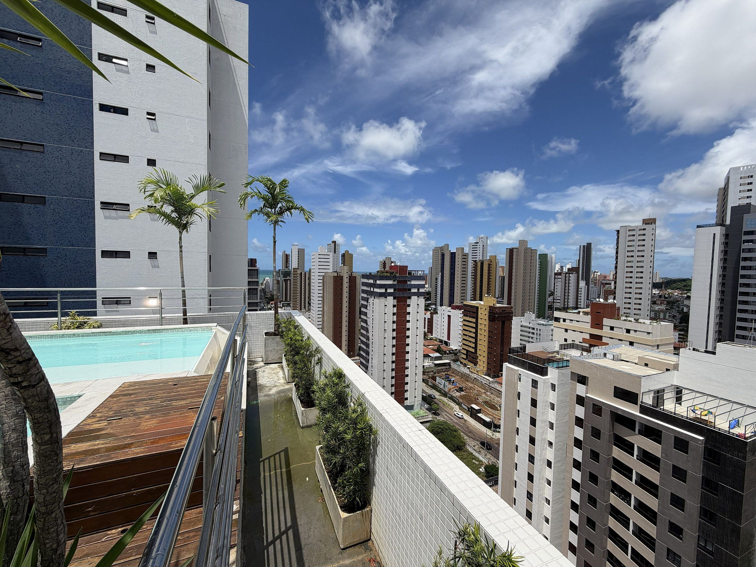 Un edificio de gran altura con piscina en la azotea, rodeado de otros edificios altos y un cielo despejado.