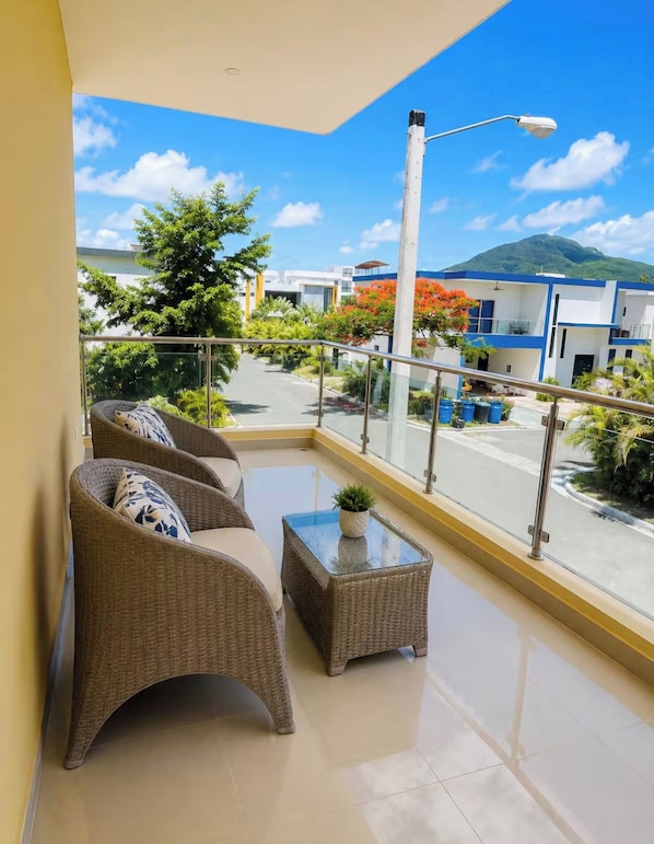 A balcony with wicker furniture, a glass-top table, and a view of a street and buildings. - Lovely House,pool,ac,near Sea,gym,bbq,puerto Silver (Montellano)