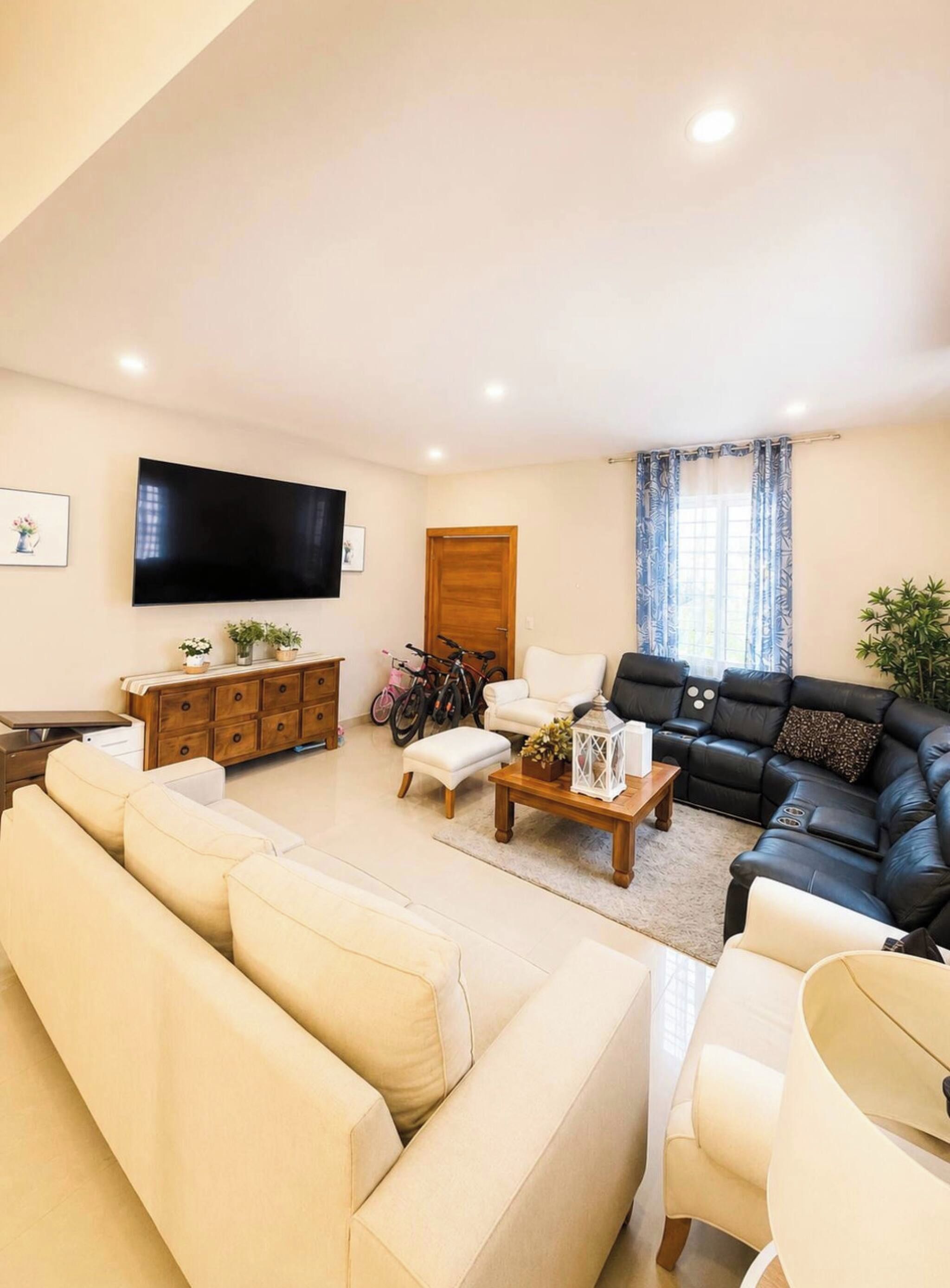 A living room with a sofa set, a coffee table, a TV mounted on the wall, and a door with a curtain.
