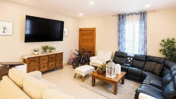 A living room with a sofa set, a coffee table, a TV mounted on the wall, and a door with a curtain.