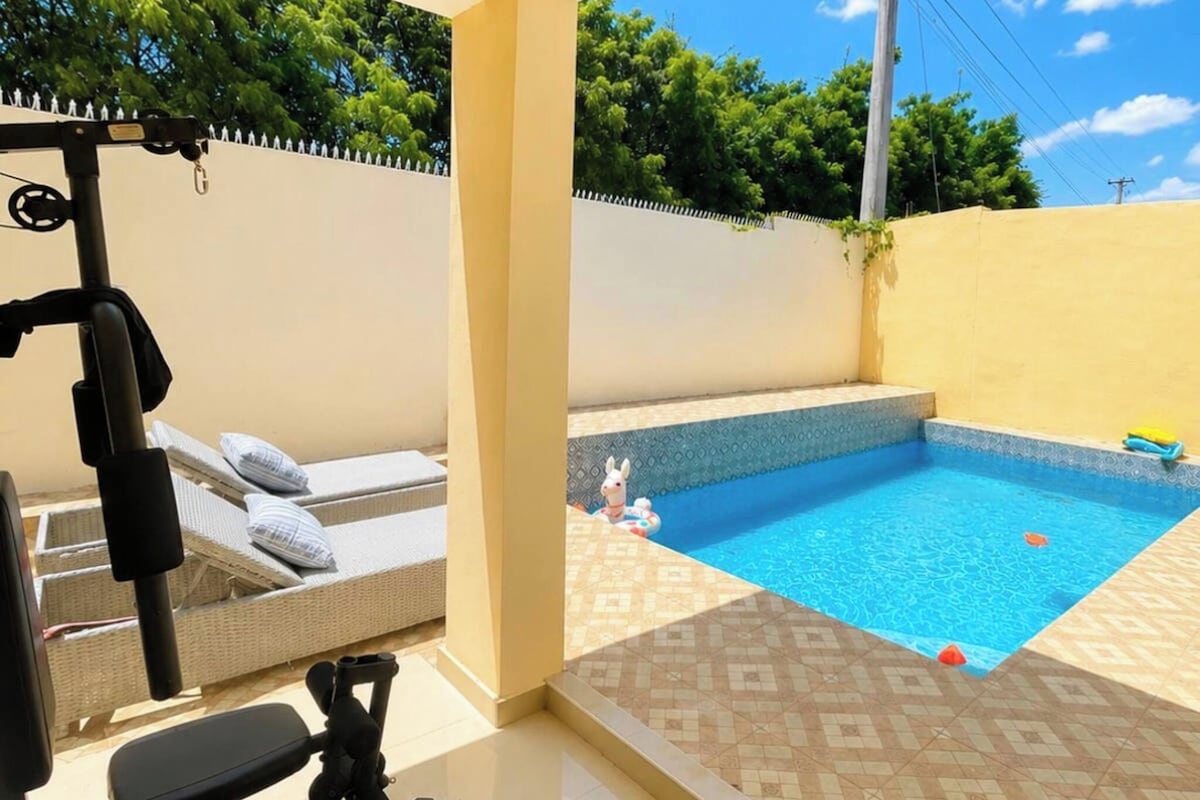 Une salle de sport équipée de matériel d’exercice et une petite piscine avec une terrasse carrelée.