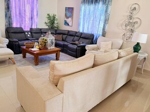 A living room with a black leather sofa, a beige sofa, a wooden coffee table with decorative items, and a green floor lamp.