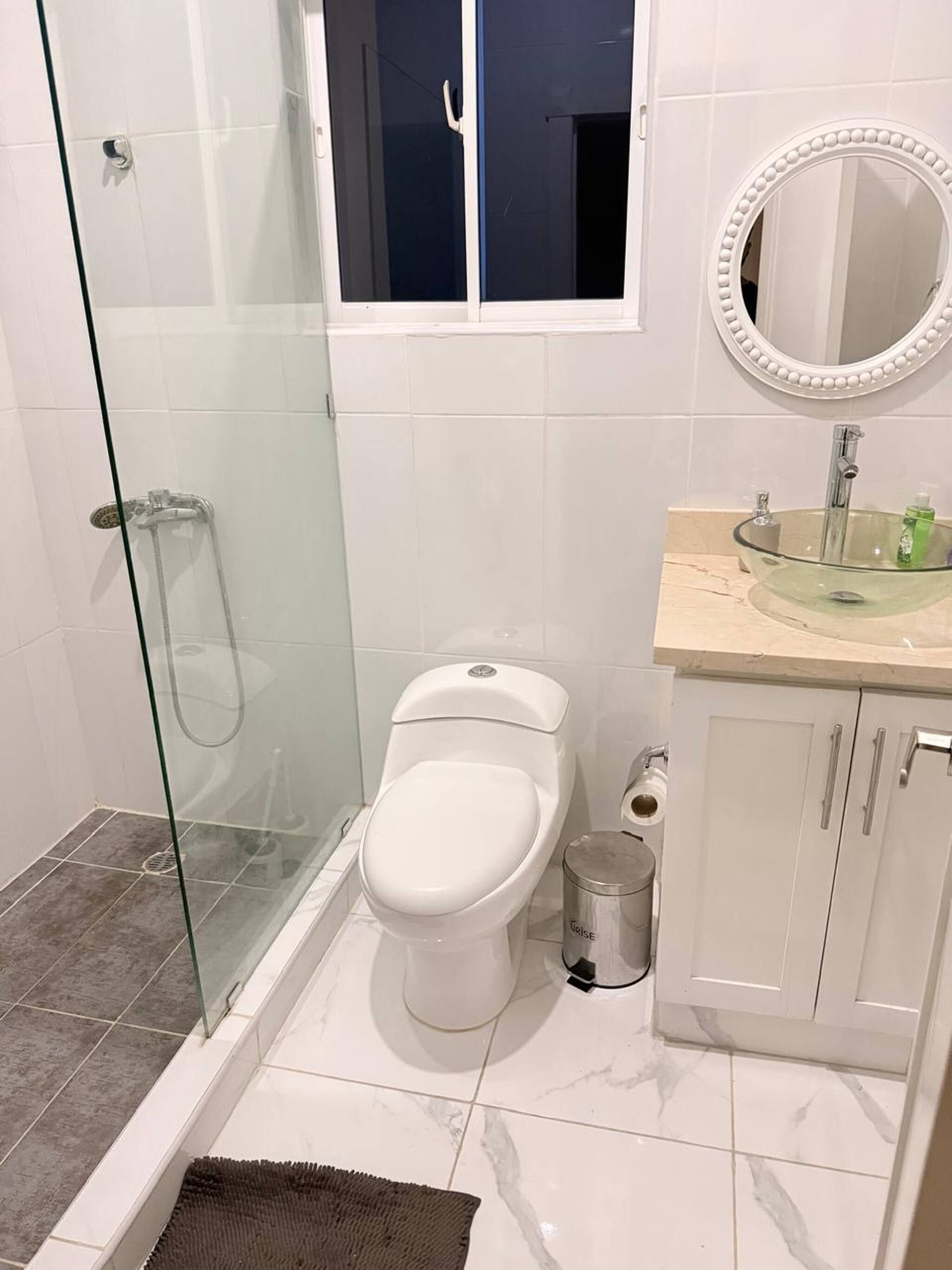 Un baño con cabina de ducha de vidrio, inodoro, lavamanos con encimera de mármol y espejo con marco decorativo.