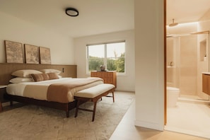 Ein Schlafzimmer mit einem Bett, einem Nachttisch, einer Bank und einem Fenster mit Blick auf Bäume.