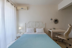 A bedroom with a bed, bedside table, lamp, desk, chair, and an air conditioning unit. - Apartment 'Cozy Home Near The Sea 12' with Balcony, Wi-Fi and Air Conditioning (Ρέθυμνο)
