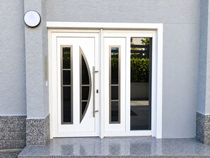 Eine Doppeltür mit gebogenem Glasspiegel, darüber eine runde Leuchte und eine strukturierte Wand.